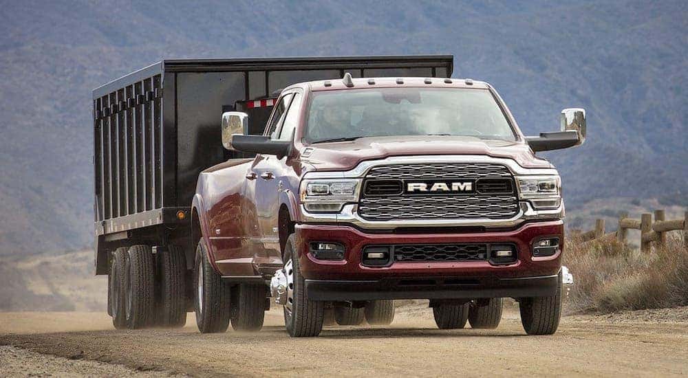 A maroon Ram 3500 is towing a trailer on a dirt road.