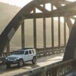 A popular used SUV for sale in Costa Mesa, a white 2019 Jeep Wrangler Unlimited is driving over a misty bridge.