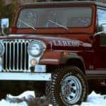 A red 1970s Jeep CJ-7 is parked in the snow.