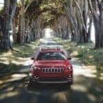One of the more confusingly named Jeep models, a red 2020 Jeep Cherokee, is shown from the front driving on a tree-lined road.