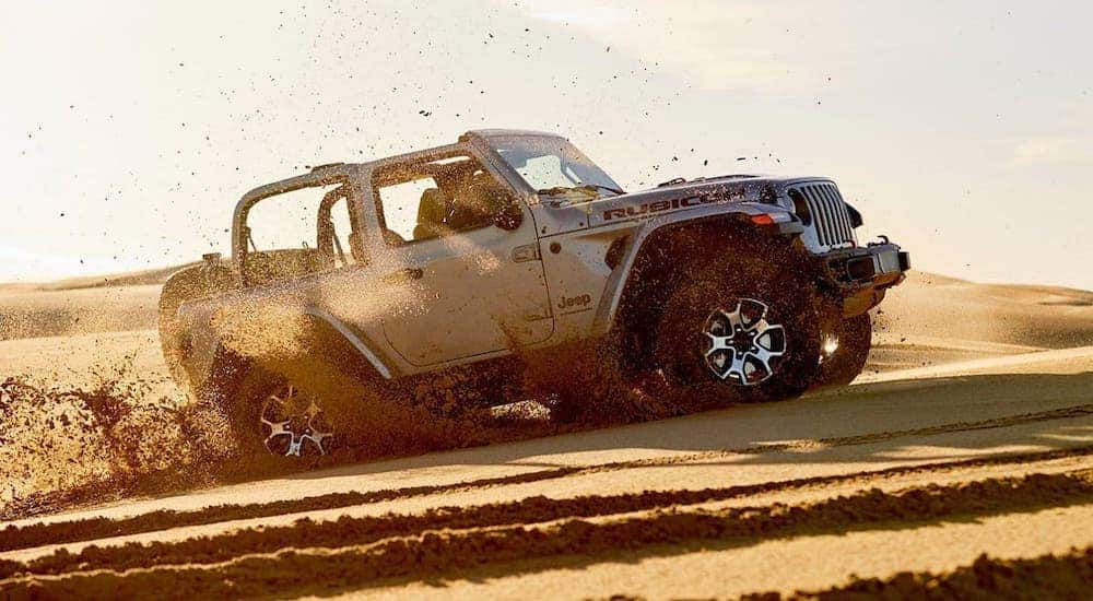 The most recognizable of the Jeep SUVs, a silver 2020 Jeep Wrangler, is kicking up sand at a beach.