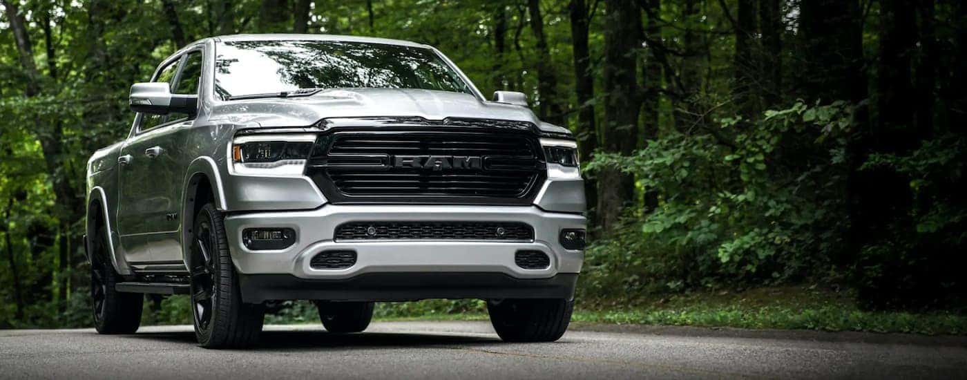 A silver 2020 Ram 1500 is driving on a tree-lined road.