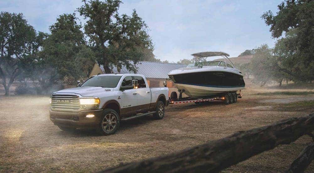 A white 2020 Ram 2500 is towing a boat on a ranch.