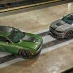 A green and a grey 2019 Dodge Challenger are parked on a stripe design on a floor, shown from above.