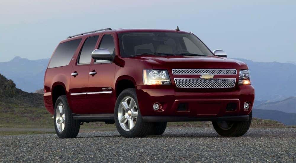 A red 2013 Chevy Suburban is parked in front of distant, hazy mountains.