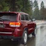 One of the best used SUVs, a red 2019 Jeep Grand Cherokee, is shown driving on a tree-lined road in the rain.