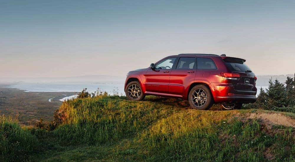 A red 2020 Jeep Grand Cherokee is parked on a hill overlooking a lake.