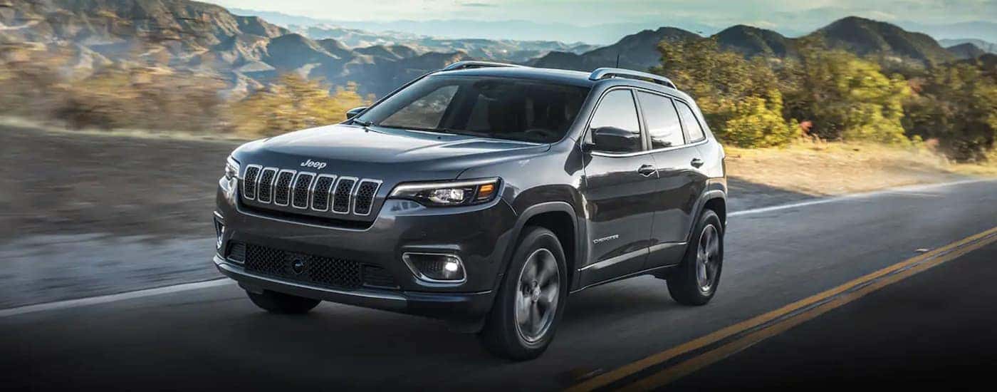 A grey 2022 Jeep Cherokee is shown from the front driving on an open road.