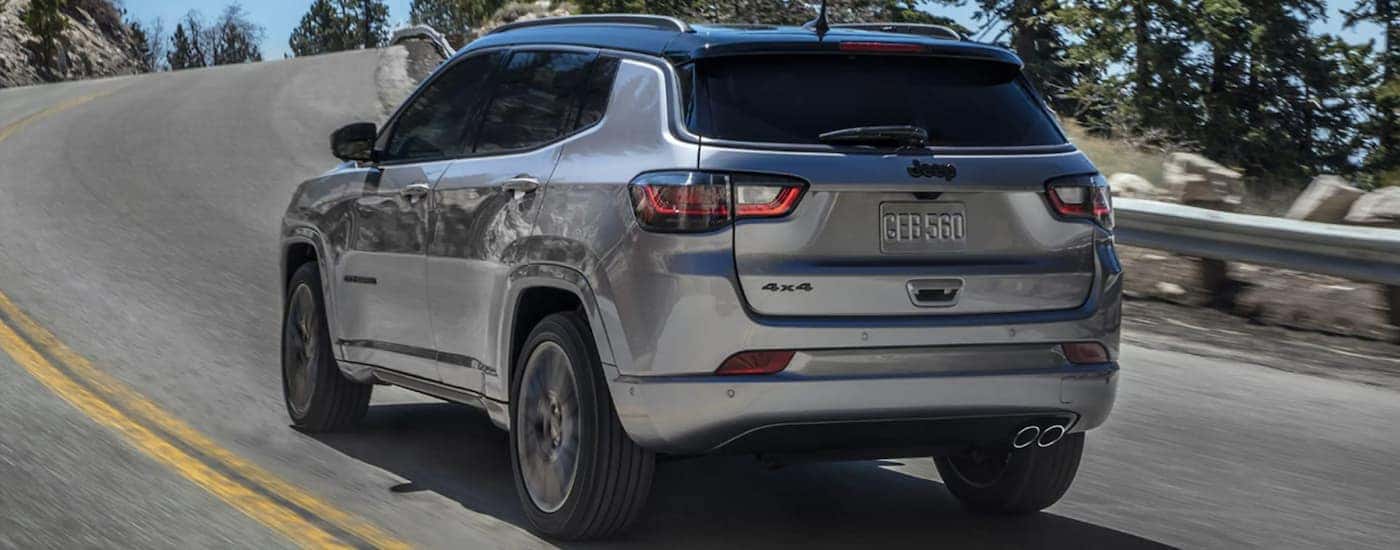 A grey 2022 Jeep Compass is shown from the rear driving on an open road.