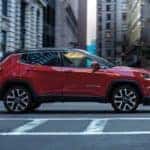 A red 2020 Jeep Compass is shown from the side driving in a city.