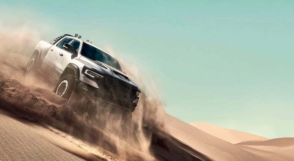 A new Ram truck for sale in Costa Mesa, a silver 2021 Ram 1500 TRX, is kicking up sand in a sand dune.