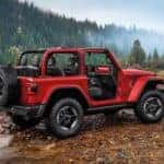 A red 2021 Jeep Wrangler with no roof or doors is crossing a river in the woods far from Costa Mesa, CA.