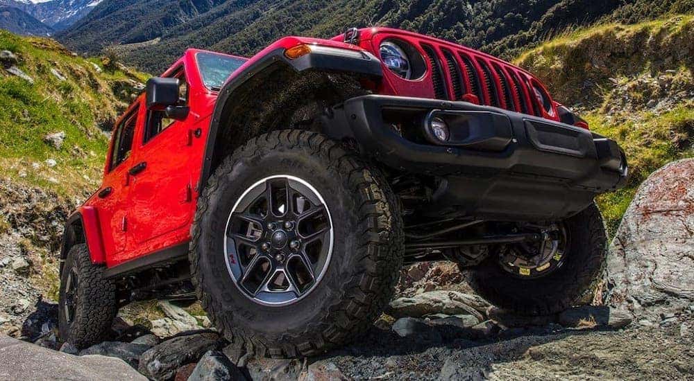 A closeup shows the wheel on a red 2021 Jeep Wrangler Unlimited with no roof climbing over rocks.