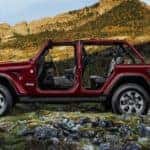 A dark red 2021 Jeep Wrangler Unlimited with no roof or doors is shown from the side while climbing a mountain.
