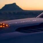 The hood of a 2021 Ram 1500 TRX is shown in closeup at dusk with a desert rock formation in the distance.