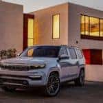 A silver 2021 Jeep Grand Wagoneer is parked in front of a modern house.