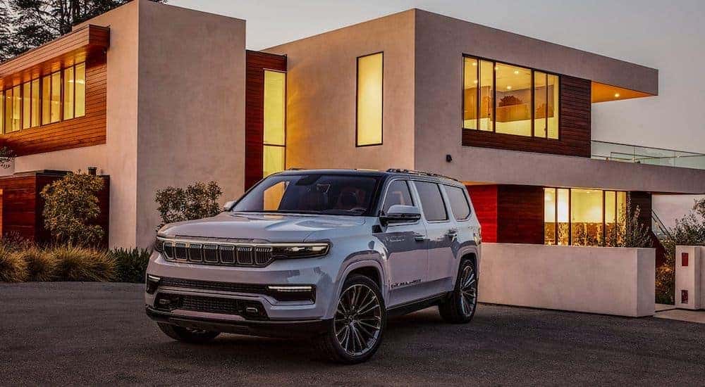 A silver 2021 Jeep Grand Wagoneer is parked in front of a modern house.