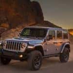 A grey Jeep Wrangler Rubicon 4xe is driving down a desert road.