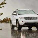A white 2021 Jeep Grand Cherokee is driving on a wet road after leaving a Jeep dealership near you.