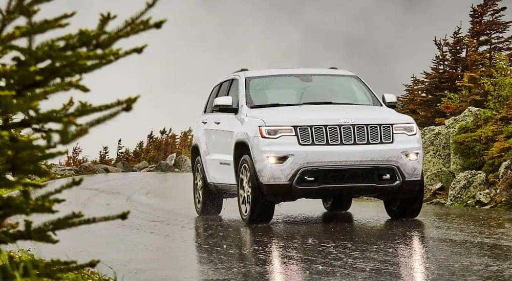 A white 2021 Jeep Grand Cherokee is driving on a wet road after leaving a Jeep dealership near you.