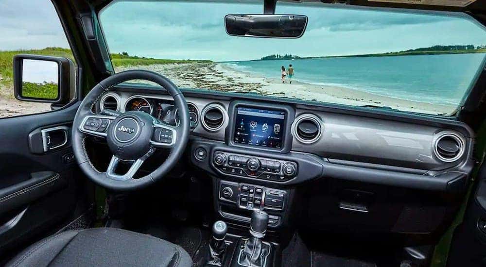 A beach with turquoise water is shown through the windshield of a 2021 Jeep Wrangler.