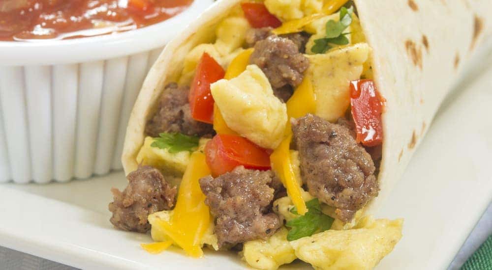 A close up is shown of a breakfast burrito and dipping sauce.