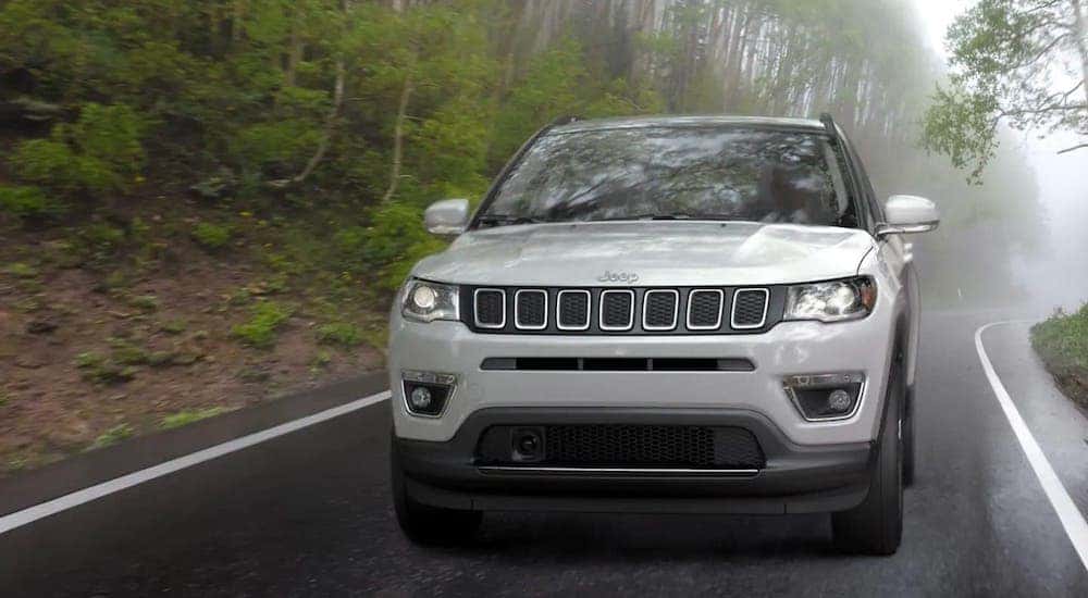 A white 2018 Jeep Compass is shown from the front while driving on a misty road.