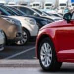 Rows of cars are shown at a used car dealer in Orange County with a red car in front.