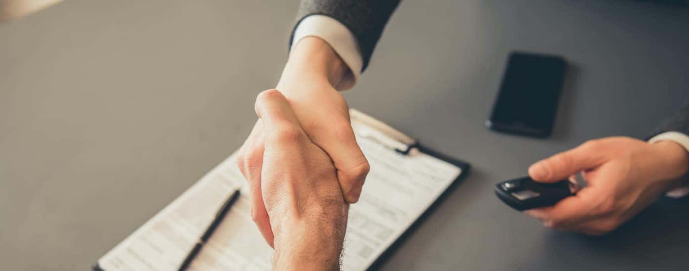 A person is shown shaking hands with a salesperson after filling out paperwork.