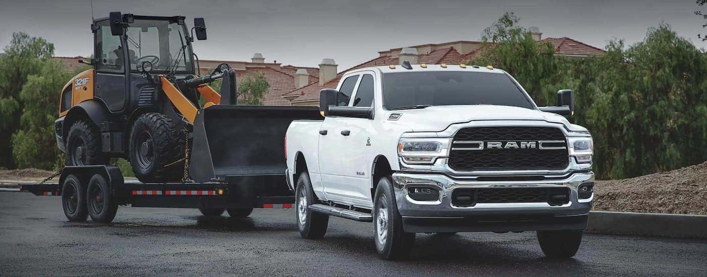 A white 2020 used Ram 2500 is towing a loader in a neighborhood.