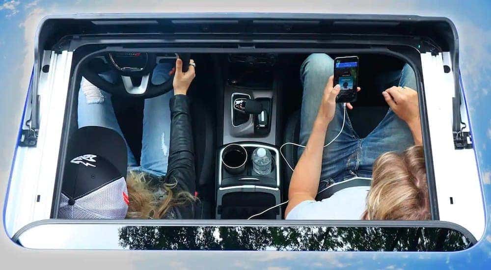 A top-down view through the moon roof of a blue 2021 Dodge Charger shows a driver and a passenger.