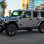 A silver 2021 Jeep Wrangler Unlimited 4xe with blue accents is driving on a highway.