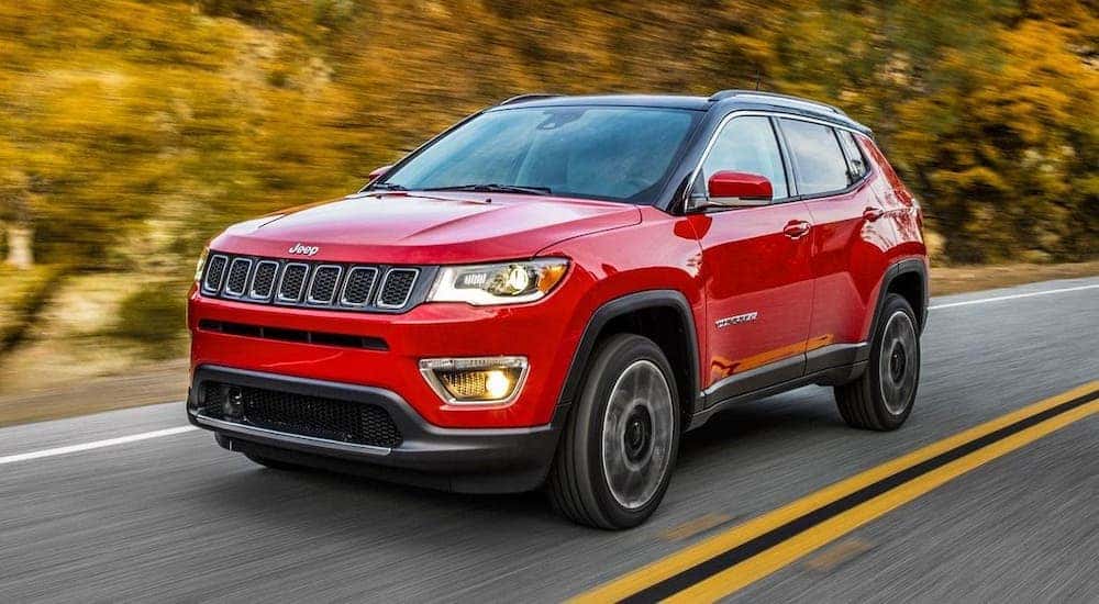 A red 2017 used Jeep Compass is driving on a highway.