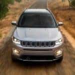 A silver 2020 used Jeep Compass is shown from the front driving on a dirt road.