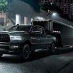 A black 2021 Ram 2500 is towing a black trailer in a city at night.