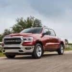 A red 2018 Ram 1500 is driving along a road next to a white fence.