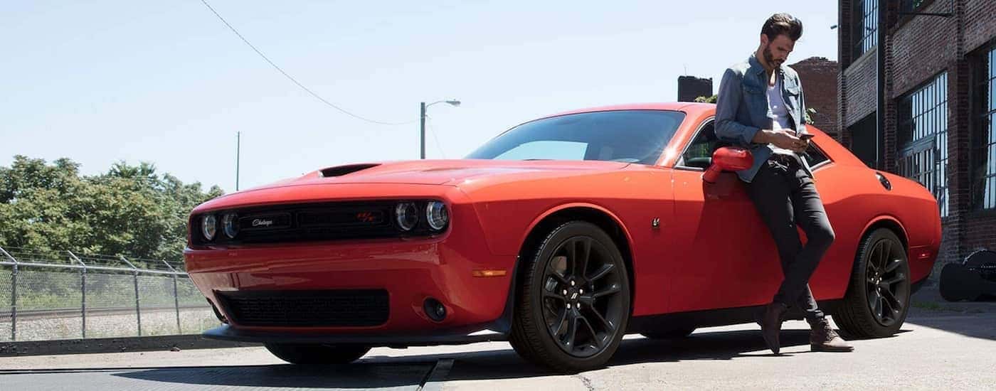 An orange 2021 Dodge Challenger Scat Pack is parked with a man leaning against it after leaving a California Dodge dealer.