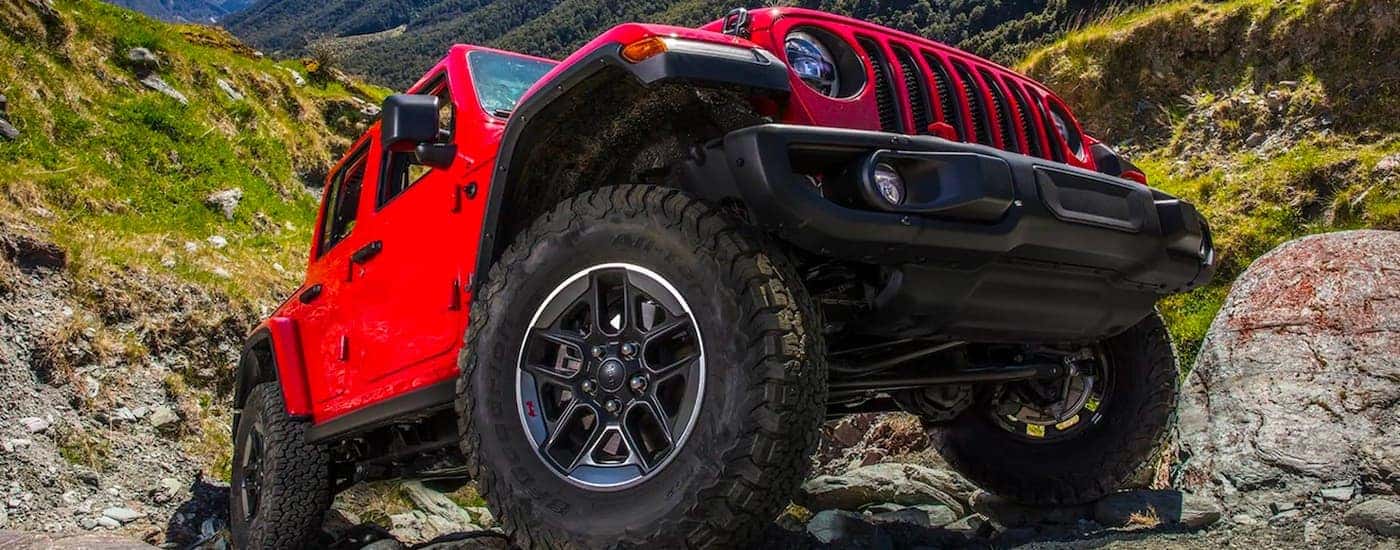 A red 2021 Jeep Wrangler Unlimited is shown from a low angle parked on rocks.