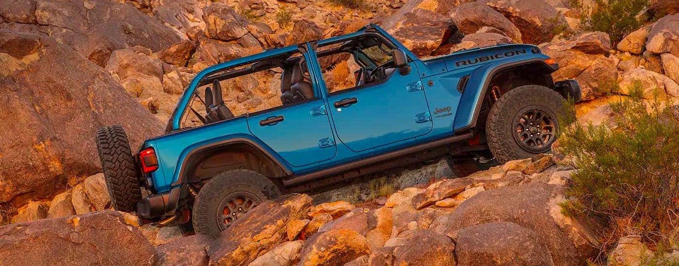 A blue 2021 Jeep Wrangler Rubicon 392 Unlimited with no roof is shown from the side climbing up a rocky hill.