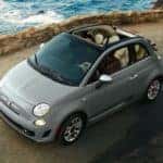A light gray 2019 used Fiat 500 is shown from a high angle driving on a coastal road.