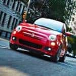 A red 2016 Fiat 500 is shown from a low angle driving on a city street after leaving a local used Fiat dealer.