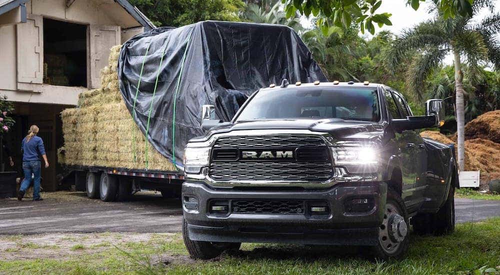 A black 2021 Ram 3500 is backing a trailer full of hay up to a barn.