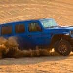 A blue 2021 Jeep Wrangler Unlimited Rubicon 392 is shown from the side kicking up sand.