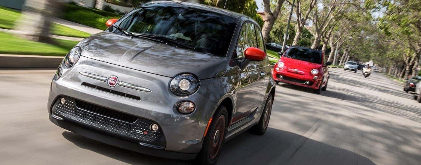 A gray and a red 2018 Fiat 500e are driving on a suburban road.