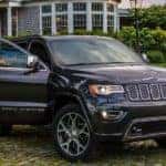 A dark gray 2020 Jeep Grand Cherokee is parked in front of a house with a person opening the passenger door.