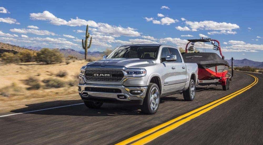 A silver 2020 Ram 1500 is towing a boat on a desert highway.