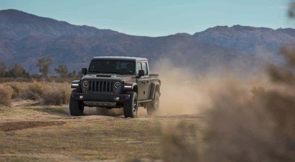 A gray 2020 Jeep Gladiator is driving in a desert in front of mountains.