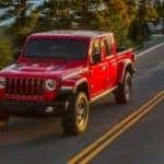A red 2020 Jeep Gladiator is driving on a highway after leaving a used pickup dealership.
