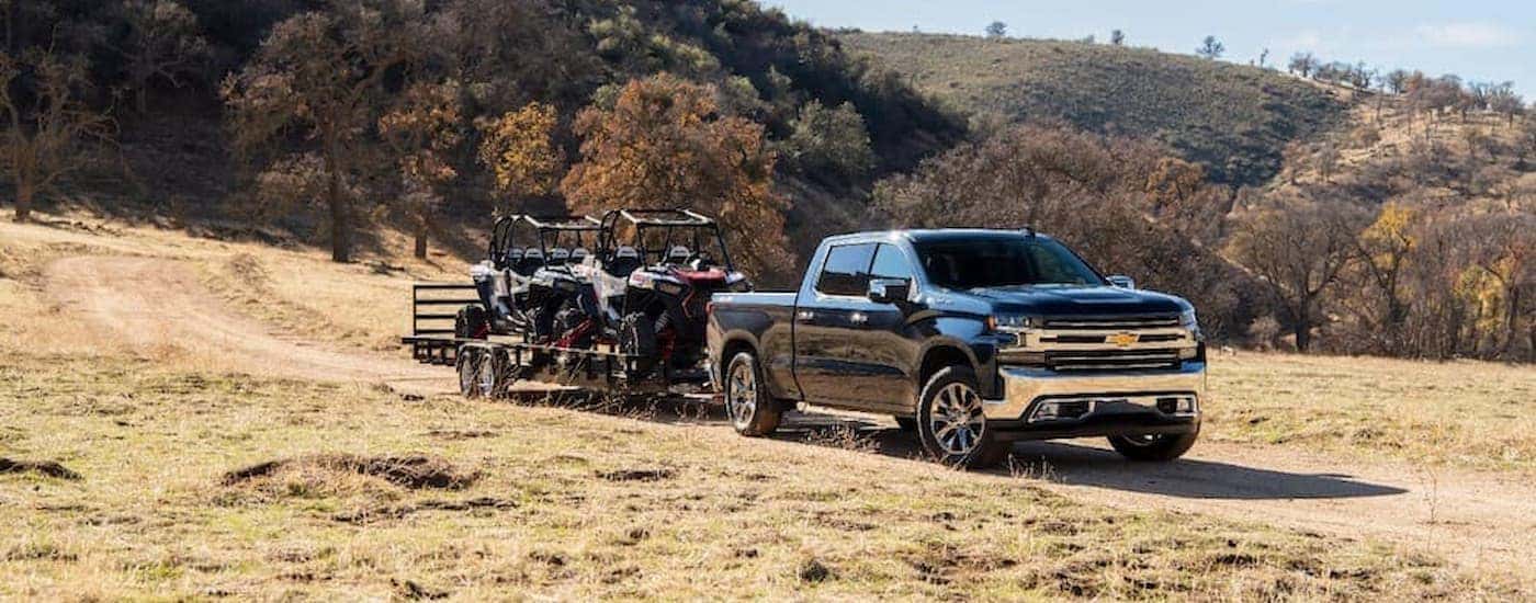 A black 2020 Chevy Silverado 1500 is shown towing ATVs through a field.