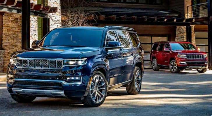 A red and a blue 2022 Grand Wagoneer are parked in front of a garage.